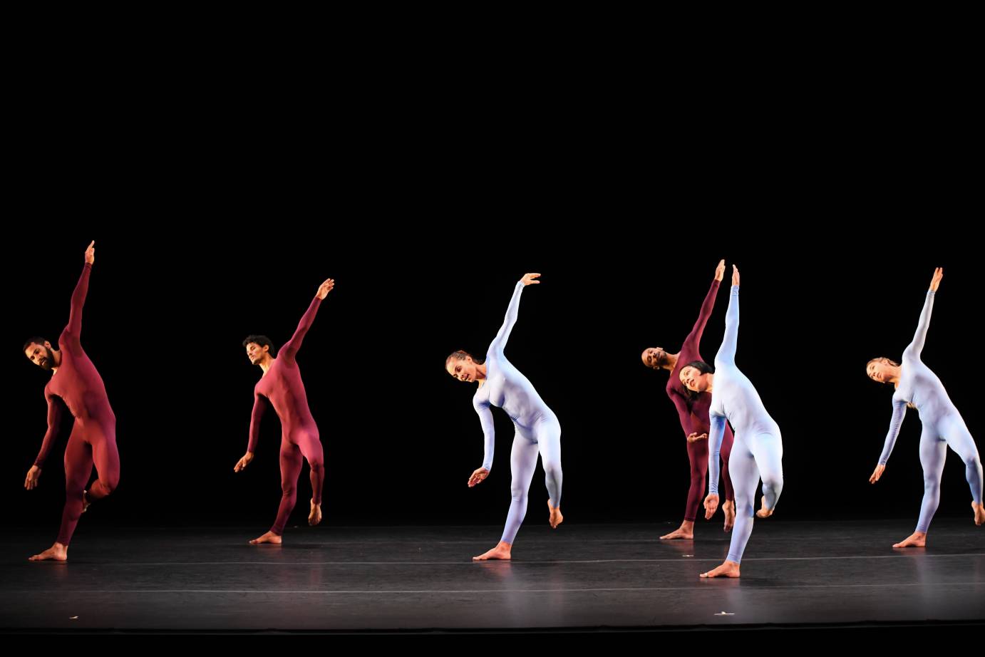 Dancers in purplish unitards tip their bodies sideways